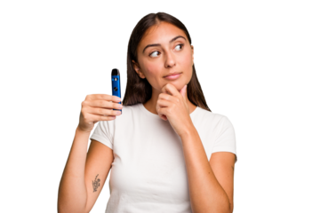Young caucasian woman holding a electronic cigarette looking sideways with doubtful and skeptical expression.