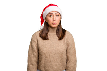 Young caucasian woman celebrating christmas wearing a santa hat isolated shrugs shoulders and open...