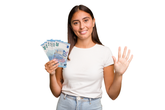 Young caucasian woman holding a banknotes isolated smiling cheerful showing number five with fingers.