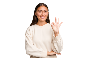 Young cute caucasian woman isolated winks an eye and holds an okay gesture with hand.