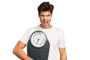 Young caucasian man holding a scale isolated screaming very angry and aggressive.