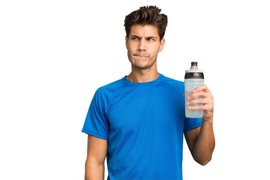 Young sport caucasian man holding a bottle of water isolated confused, feels doubtful and unsure.