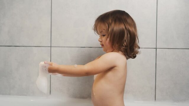 A cute two-year-old girl is playing with foam in the bathroom