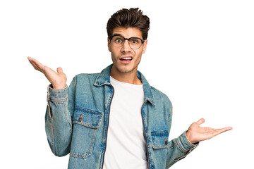 Young caucasian handsome man isolated confused and doubtful shrugging shoulders to hold a copy...