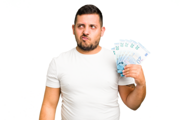 Young caucasian man holding a banknotes isolated confused, feels doubtful and unsure.