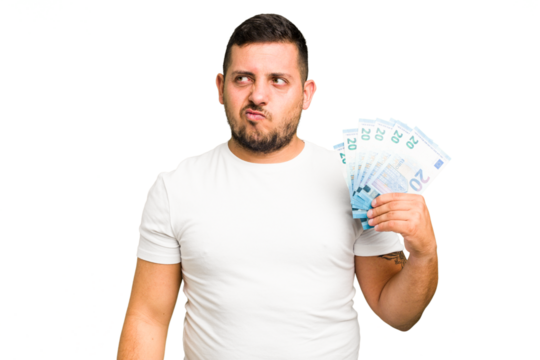 Young caucasian man holding a banknotes isolated confused, feels doubtful and unsure.