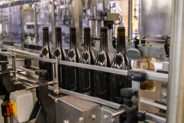 Dark glass bottles being filled with wine by industrial bottling machine at modern wine factory