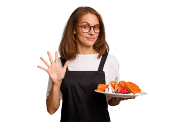 Young caucasian woman holding a waffles dish isolated smiling cheerful showing number five with fingers.