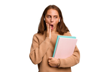 Young student woman holding a books isolated is saying a secret hot braking news and looking aside