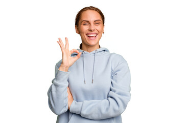 Young caucasian woman isolated winks an eye and holds an okay gesture with hand.