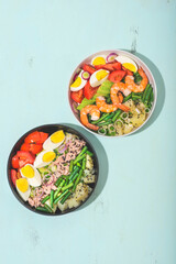 Gluten free poke or seafood salad bowl with vegetables and potatoes on the blue background. Tuna, shrimp, potatoes, avocados, eggs, tomatoes, green beans. Healthy dinner, lunch, Earth tones, top view