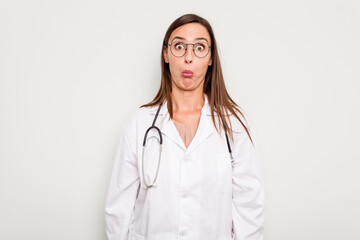 Young doctor woman isolated on white background shrugs shoulders and open eyes confused.