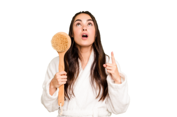 Young caucasian woman holding shower brush isolated on green chroma background pointing upside with opened mouth.