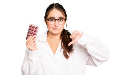 Young pharmacist woman holding a pills isolated on green chroma background showing a dislike gesture, thumbs down. Disagreement concept.