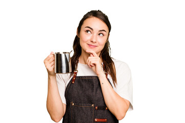 Young barista woman isolated on green chroma background looking sideways with doubtful and...