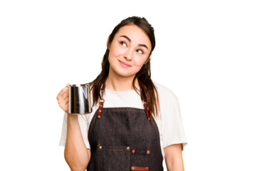 Young barista woman isolated on green chroma background dreaming of achieving goals and purposes