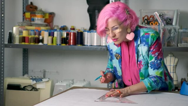 Dressmaker with pink hair and colorfull clothes drawing sewing patterns in a sewing workshop.