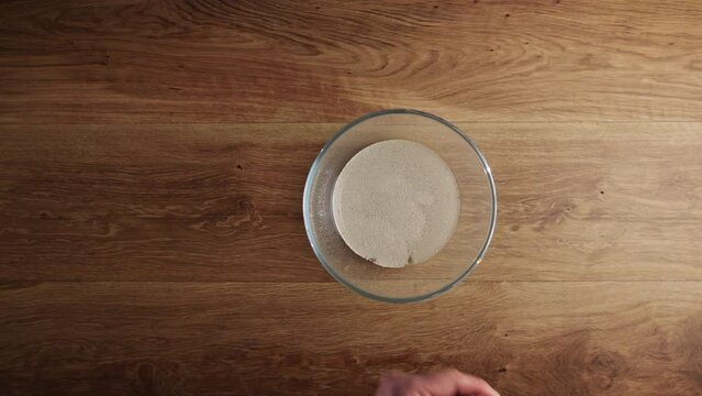 Home chef mixing dry yeast with water in a glass mixing bowl.