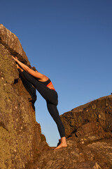 vertical shot of mature woman doing stretching on rock in golden sunrise light