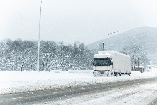 Big commercial semi-trailer truck trapped in snow drift on closed highway road at heavy snow storm blizzard cold winter day. Cargo vehicle stuck on freeway at bad weather conditions frosty snowfall