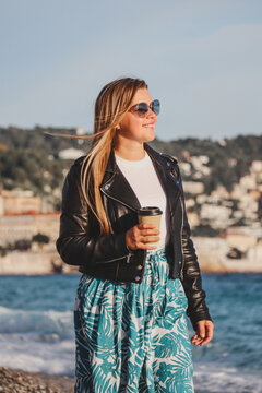 Young beautiful girl with coffee on an autumn sunny day walks on the beach of the Mediterranean Sea