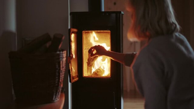 Blonde woman folding logs in the traditional wood-burning furnace. Cosy winter evenings and romantic fireplace light. Heating season in the cold mountains.
