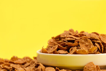 Durum wheat flakes - quick breakfast cereal on a plate on a yellow background, space for text.