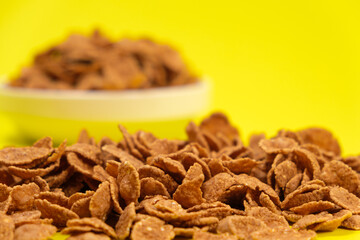 Close-up of wheat flakes on yellow background, quick cereal healthy breakfasts.