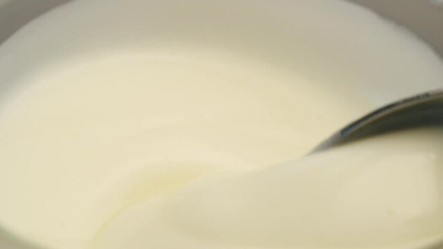 Macro of mixing yogurt with a spoon in a cup.
