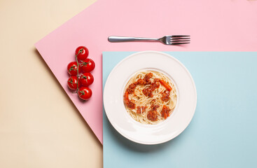 top view of pasta with meat in white plate near fork and cherry tomatoes on pink, blue, beige background
