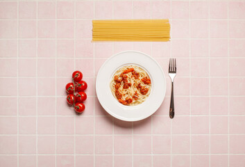 top view of pasta with meat in white plate near fork and cherry tomatoes on pink background