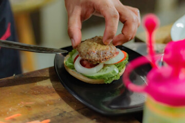 Chef puts beef patty for burger filling, on kitchen utensils background