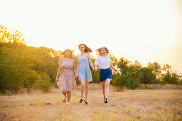 Fototapeta premium A group of girlfriends jumps and runs outdoors. A group of female friends hugs and enjoys the sunset in nature. Laughter, smiles and joy.
