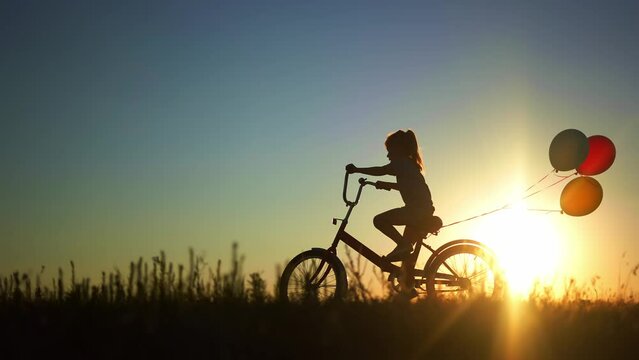 girl kid silhouette bike riding on a park. kid girl rides a bike in nature in the park on the road. happy family kid dream concept. daughter plays a bike rides on a sandy road lifestyle