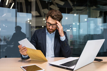 Sad and upset mature businessman received an envelope by mail with a bad news notification letter,...