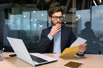 Sad and upset mature businessman received an envelope by mail with a bad news notification letter,...