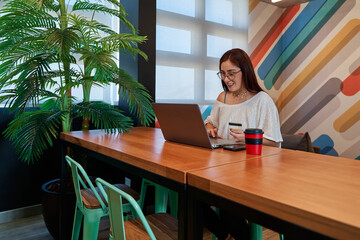 young red haired woman with card in hand to shop online with her laptop at a community space