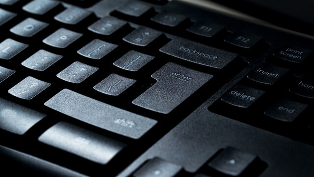 Detail view of desktop computer keyboard with light shining on keys. Enter key on keyboard. Night work. Macro. Selective focus.