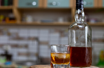Whiskey glass with ice cubes, misted bottle on wooden table
