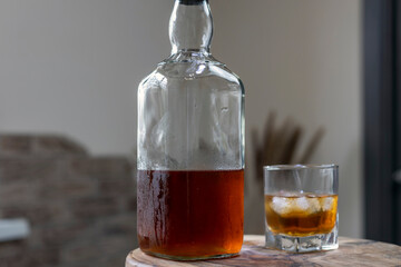 Glass of whiskey on ice with bottle on wooden bar