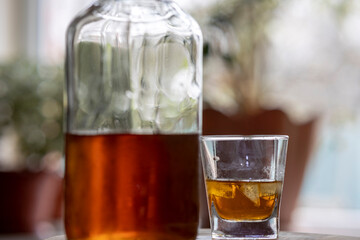 Whiskey glass with ice cubes, misted bottle on wooden table