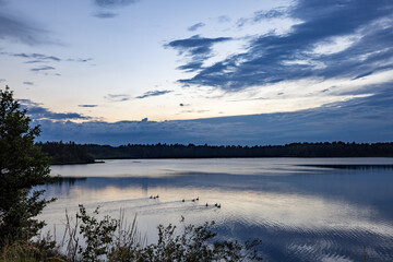 a beautiful blue lake with green tree in the foreground under a dramatic blue dusk sky. High quality photo