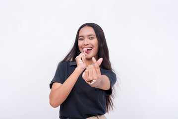 A young upbeat asian woman makes a finger heart sign while holding a lollipop. Isolated on a white background. - Powered by Adobe
