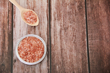 Obraz na płótnie Canvas small granules of natural Himalayan salt in a wooden spoon and a decorative metal plate on a wooden background