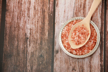 small granules of natural Himalayan salt in a wooden spoon and a decorative metal plate on a wooden background