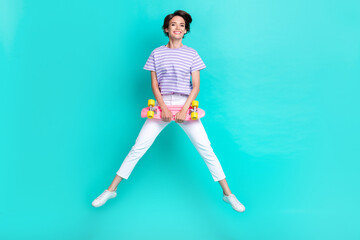 Full length photo of pretty cute lady wear violet t-shirt holding skate jumping high isolated turquoise color background