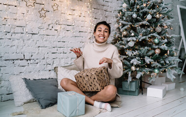 Fototapeta na wymiar Woman opening gift near Christmas tree at home