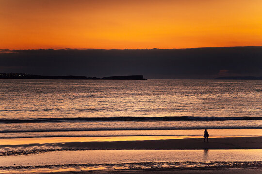 Person walking in the distance next to the sea during sunset on the beach.Orange and golden sunset. Peniche beach. Portugal, Europe.