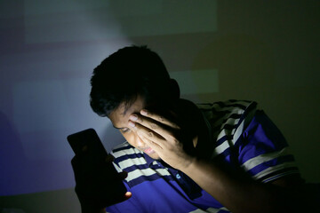 young man on bed using smart phone at night suffering eye pain 