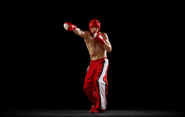 Studio shot of male kickboxer, mma fighter in motion and action isolated over dark background. Muay...